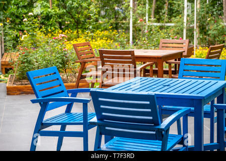 Pont en bois bleu et marron, chaise et table set dans le jardin avec des fleurs colorées en arrière-plan sur le terrain. Banque D'Images