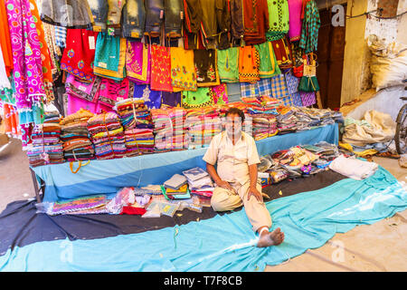 Exposant assis à un décrochage à vendre des tissus dans un marché couvert à Shahpura, Dindori district de l'état indien de Madhya Pradesh Banque D'Images