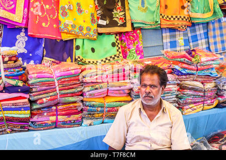 Exposant assis à un décrochage à vendre des tissus dans un marché couvert à Shahpura, Dindori district de l'état indien de Madhya Pradesh Banque D'Images