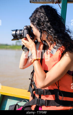 Jeune femme blanc portant un gilet de prendre des photos en allant sur un bateau sur la rivière Madre de Dios, rivière, bassin de l'Amazone, au Pérou Banque D'Images