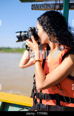 Jeune femme blanc portant un gilet de prendre des photos en allant sur un bateau sur la rivière Madre de Dios, rivière, bassin de l'Amazone, au Pérou Banque D'Images