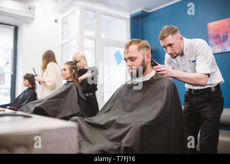 Gros plan d'un homme d'obtenir un coupe très tendance à un salon de coiffure. Portrait masculin coiffure desservant un client. Homme barbu avec une décote de t Banque D'Images