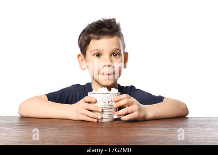 Cute little boy avec tasse de cacao chaud boire assis à table contre fond blanc Banque D'Images