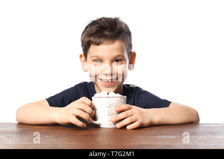 Cute little boy avec tasse de cacao chaud boire assis à table contre fond blanc Banque D'Images