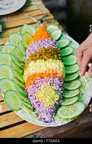 Thon frit recouvert d'oignons, carottes et fromage présenté sur une assiette décorée avec des tranches de concombre. C'est un plat originaire des Philippines Banque D'Images