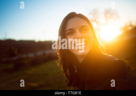 Jolie jeune femme en riant avec le coucher du soleil derrière elle Banque D'Images