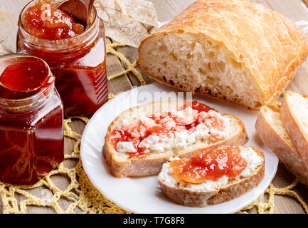 Close-up toasts avec caillé et fraise sucrée et confitures apple sur plaque blanche et ouvrir les bocaux en verre de confiture sur la serviette sur tricoté jaune en bois rustique tabl Banque D'Images