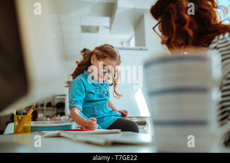 Girl robe denim peinture sur la table de travail de mère Banque D'Images