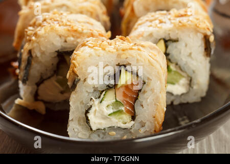 Close up avec Uramaki Conger. Rouleaux de sushi avec nori, riz, anguille poisson, fromage, morceaux d'avocat, concombre, saumon décoré de graines de sésame sur cerami Banque D'Images
