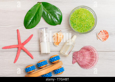 Les bouteilles avec de la crème pour visage peau et aromatiques, l'huile de massage à la main, bol avec sel de mer, étoiles de mer et les coquillages sur fond de bois gris. Un des produits de spa Banque D'Images