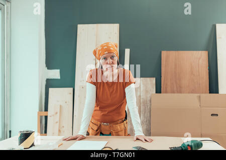 Female carpenter avec bandana posant dans l'atelier de menuiserie, petite entreprise au lieu de travail Banque D'Images