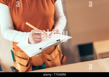 L'auto-portrait utilisé female carpenter writing project notes sur le bloc-notes de presse-papiers dans la petite entreprise de papier l'atelier de menuiserie Banque D'Images