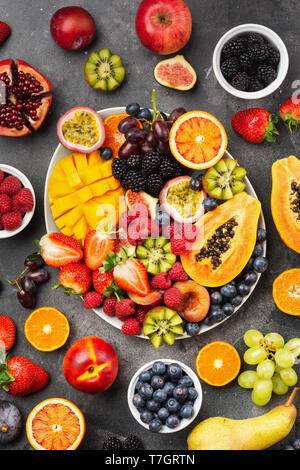 Plateau de fruits délicieux grenade mangue papaye framboises fruits de la passion oranges sur une assiette ovale de petits fruits sombres sur fond de béton, selecti Banque D'Images