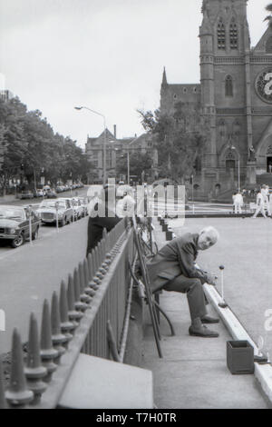 1977 Sydney, Australie : Les hommes regarder par-dessus la clôture et de l'intérieur de l'ex-Lawn Bowls vert sur la rue College. Le club de pétanque a été créé en 1880 et supprimé dans le cadre d'une rénovation majeure de la zone en face de la cathédrale St Mary, représenté à l'arrière-plan. Les rénovations comprenaient une piscine publique complexe et une grande zone pavée en face de la cathédrale. Banque D'Images