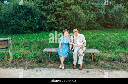 Les grands-parents et petit-fils posant pour une photo assise sur un banc à l'extérieur Banque D'Images