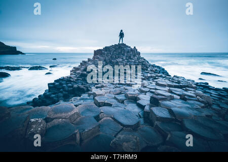 Une personne debout sur les rochers au bord de la mer à la Giant's Causeway, l'Irlande du Nord. Banque D'Images