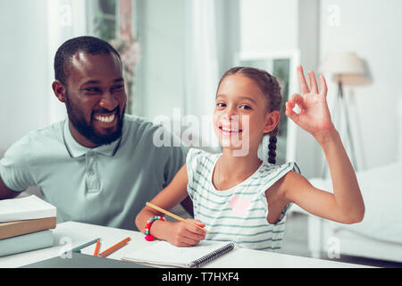 Happy girl montrant le signe ok pendant que papa assis près de. Banque D'Images