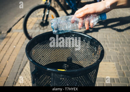 La main de femme jette une bouteille d'eau en plastique vide en ville rue corbeille sur sunny day, close-up Banque D'Images