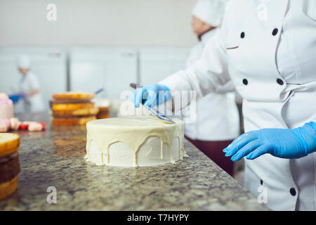 Mains crème confiseur s'étend sur un gâteau blanc sur la table dans la pâtisserie Banque D'Images