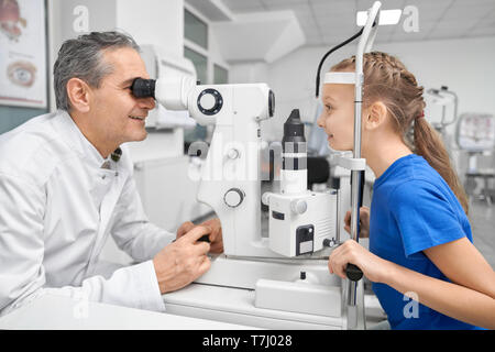 Médecin Professionnel low angle yeux de joli patient à l'aide de lampe à fente. Spécialiste de l'œil en blanc manteau médicale à la recherche grâce à un équipement spécial. Concept d'une saine vision. Banque D'Images