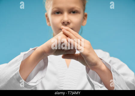 Focus sélectif de petites mains de fille montrant le poing en studio. Enfant mignon femelle looking at camera et posant sur fond bleu isolé. Jeune combattant de la formation et de faire le karaté. Concept de sport. Banque D'Images