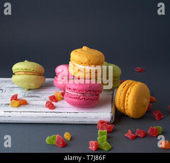 Des gâteaux multicolores de la farine d'amande macarons sur une planche de bois blanc, fond noir Banque D'Images