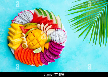 Assortiment de fruits tropicaux sur une plaque blanche avec feuille de palmier. Fond bleu. Vue d'en haut. Copier l'espace. Banque D'Images
