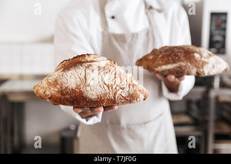 Image de l'homme en uniforme blanc Baker au permanent et boulangerie Pain holding Banque D'Images