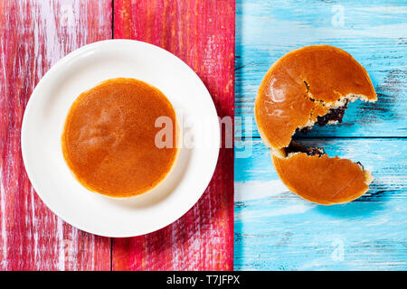 Portrait de deux dorayaki, une pâtisserie remplie de pâte de haricots adzuki typique de Japon, bleu et rouge sur une table en bois rustique Banque D'Images