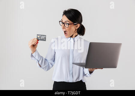 Portrait of smiling businesswoman wearing eyeglasses holding silver ordinateur portable et une carte de crédit au bureau isolé sur fond blanc Banque D'Images
