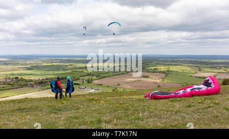 Devils Dyke, Sussex, UK ; 6 mai 2019 ; Hommes et femmes avec leur voile de parapente sur le terrain. Deux parapentes volent derrière eux Banque D'Images