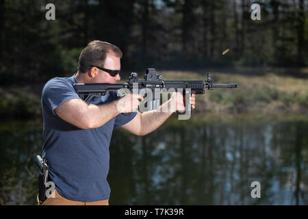 Un homme le tir à la cible avec un fusil d'assaut et la shell éjecté en l'air. Banque D'Images