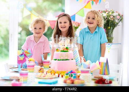 Kids Birthday party. Les enfants de souffler les bougies sur le gâteau lapin rose. Arc-en-ciel pastel et décoration de table pour les enfants, l'événement de bannière et de drapeau. Une fille Banque D'Images