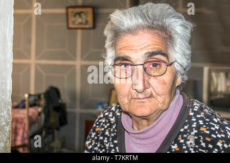 Une vieille femme avec des lunettes se penche sur l'objectif du photographe derrière sa photo sur le mur Banque D'Images