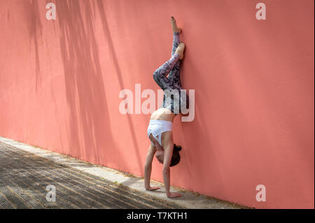 Woman doing handstand un contre un mur rose saumon dehors au soleil Banque D'Images