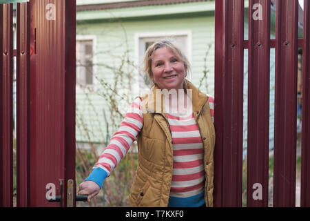 Mature Woman l'ouverture de la barrière rouge d'accueillir quelques invités. Banque D'Images