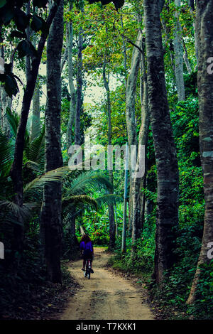 Fille sur un vélo le long d'un chemin au milieu de la forêt tropicale à Havelock, Île-de-France Banque D'Images