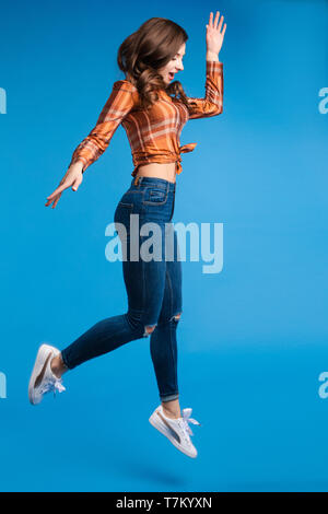 Cool jeune et belle brunette girl in checked shirt attachées à l'avant et jeans slim avec des baskets sautant en l'air. Elle est active et énergique. Est Banque D'Images