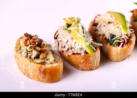 Brushetta défini pour un apéritif. Variété de petits sandwiches avec tomates, fromage parmesan, avocat et noix servi sur un fond blanc Banque D'Images