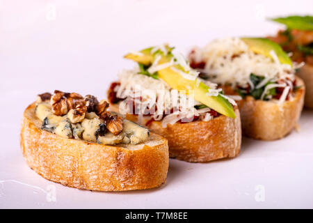 Brushetta défini pour un apéritif. Variété de petits sandwiches avec tomates, fromage parmesan, avocat et noix servi sur un fond blanc Banque D'Images