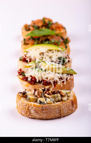 Brushetta défini pour un apéritif. Variété de petits sandwiches avec tomates, fromage parmesan, avocat et noix servi sur un fond blanc Banque D'Images