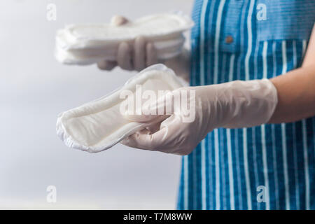 Produits d'hygiène de la femelle. Femme gants médicaux en tenant une pile de serviettes sanitaires contre l'arrière-plan blanc. Période jours concept montrant femin Banque D'Images