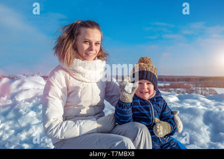 Une jeune mère avec un jeune fils d'un garçon de 4 ans. Se trouve dans l'hiver contre la neige et le ciel. Jouer à l'extérieur dans le week-end des vacances. Banque D'Images