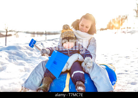 Jeune mère et son petit garçon de 3 ans. En hiver, en descendant une colline sur un fond de neige. Vacances en vacances d'hiver. Relations sérieuses in joy émotions Banque D'Images