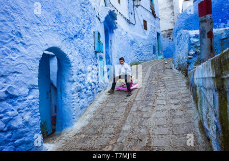 Chefchaouen, Maroc : Un enfant joue avec une forte Lane dans le bleu à la chaux medina vieille ville. Banque D'Images