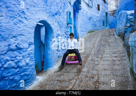 Chefchaouen, Maroc : Un enfant joue avec une forte Lane dans le bleu à la chaux medina vieille ville. Banque D'Images