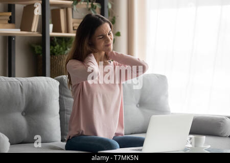 Femme assise sur la table près de l'ordinateur souffre d'une douleur au cou Banque D'Images