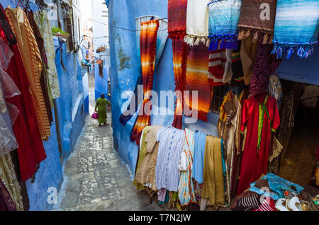Chefchaouen, Maroc : une femme passe devant un magasin de vêtements dans le bleu à la chaux medina vieille ville. Banque D'Images