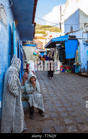 Chefchaouen, Maroc : deux hommes portant des djellabas siéger dans le bleu à la chaux ruelles de la médina, vieille ville. Banque D'Images
