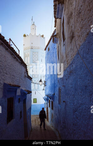 Chefchaouen, Maroc : un homme marche dans une ruelle lavés sous le minaret d'une mosquée dans la médina. Banque D'Images